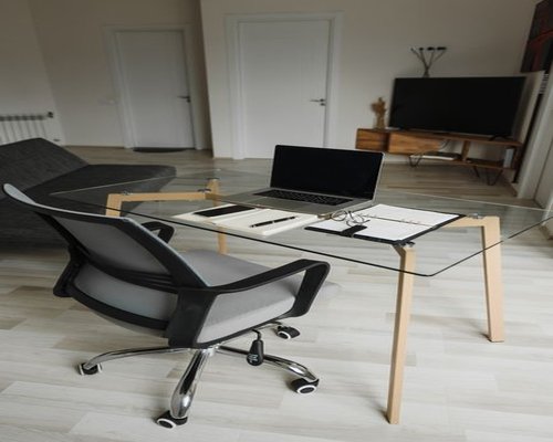 Ergonomic office setup with a well-positioned wooden table, comfortable mesh chair, laptop stand, and glass of water under bright daylight